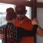 A man in an orange shirt and a black hat dancing with a woman