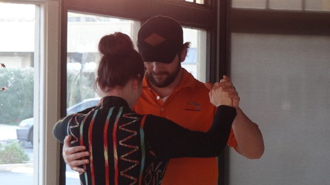 A man in an orange shirt and a black hat dancing with a woman